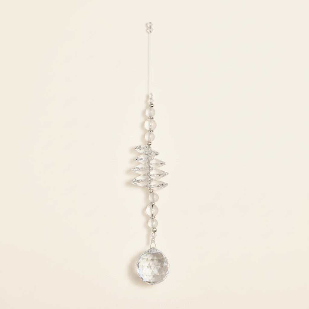 A clear crystal wind chime ornament with a hanging tag, displayed on a brown wooden floor.