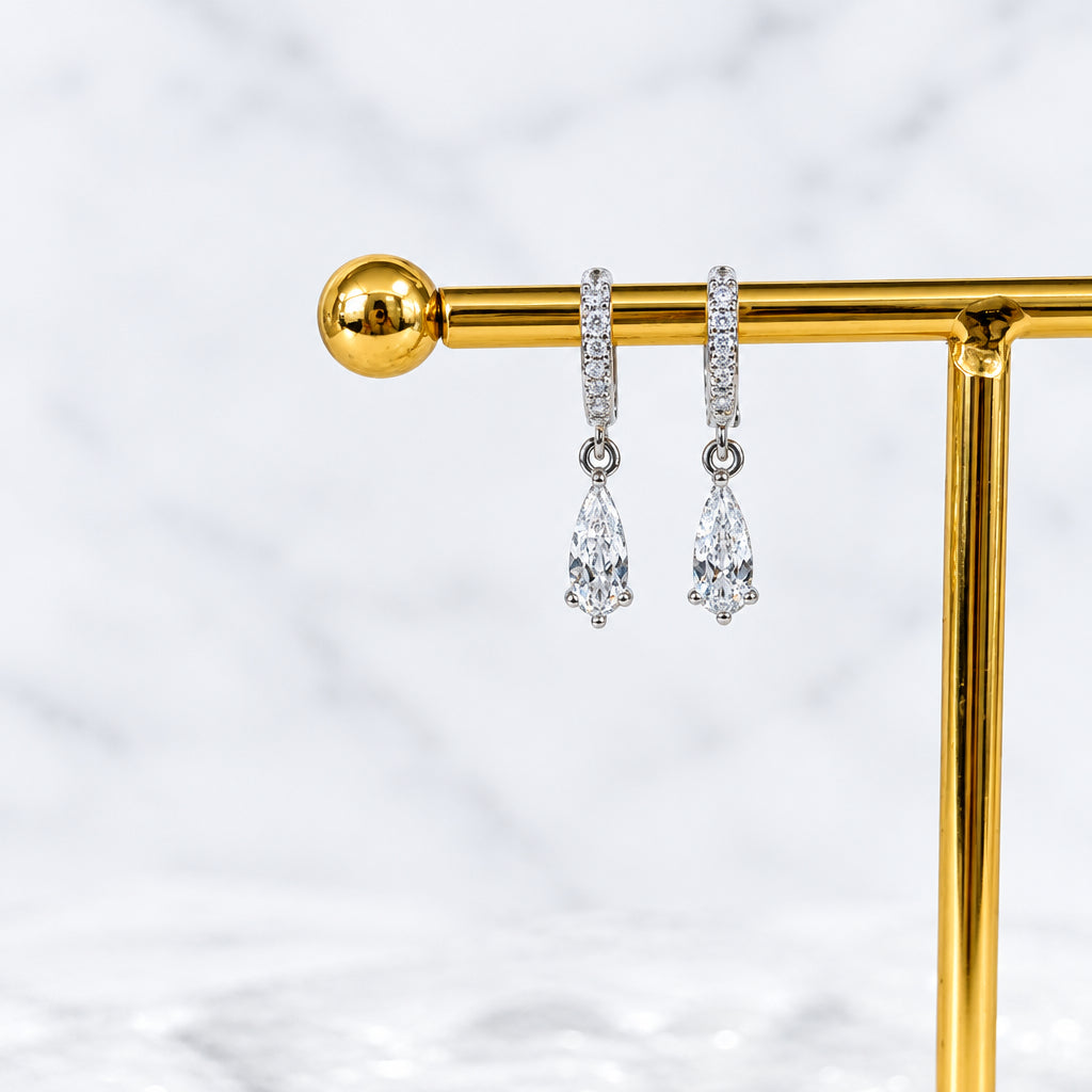 Silver teardrop earrings on a gold stand with a white stone background