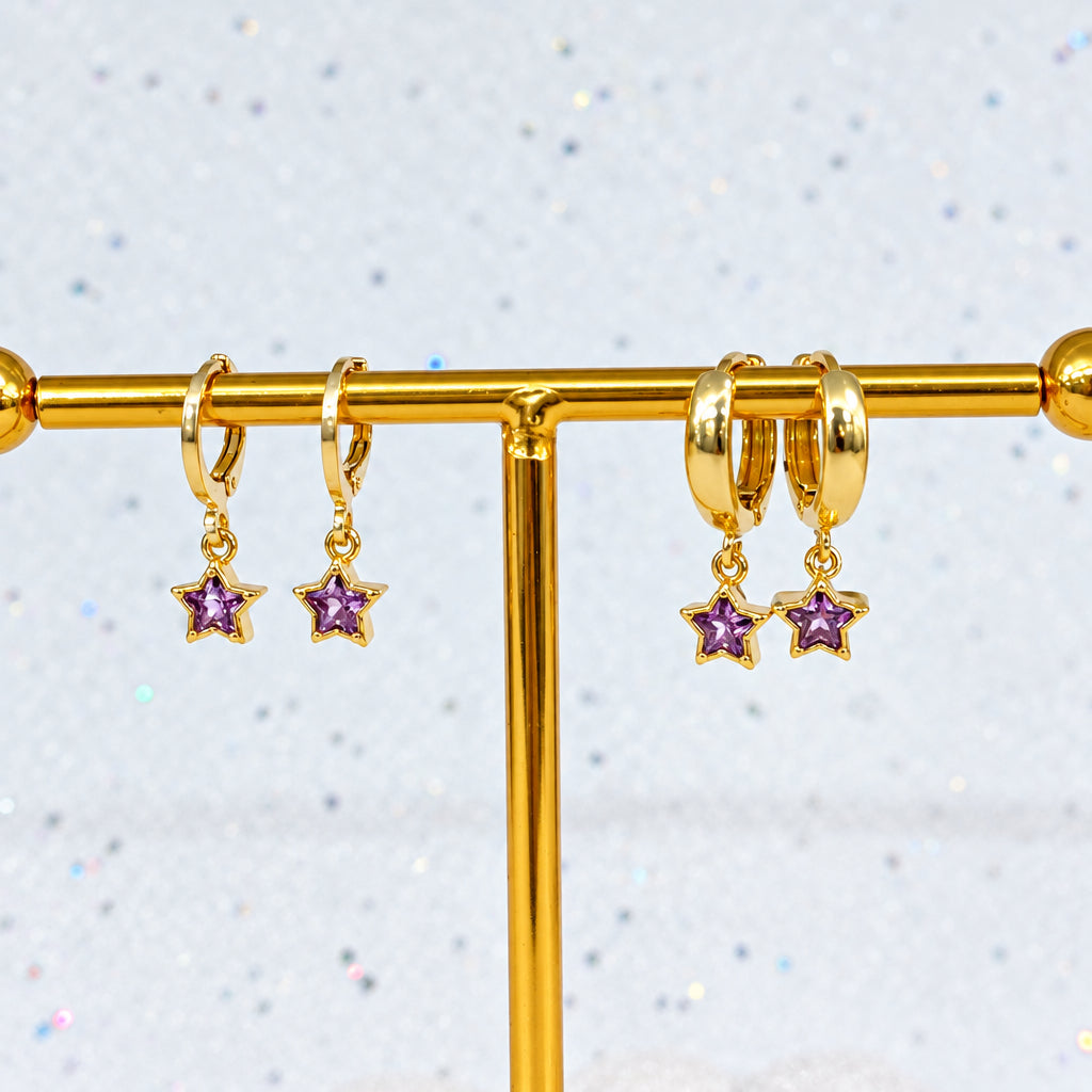 Gold hoop earrings with star charms on a gold stand against a light gray background