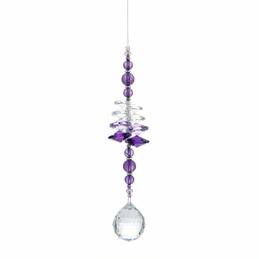 A beaded hanging ornament or suncatcher with purple and clear crystals, suspended against a wooden background.