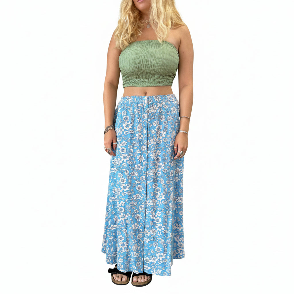 Person wearing a green top and blue floral skirt in a store setting with plants and shelves.