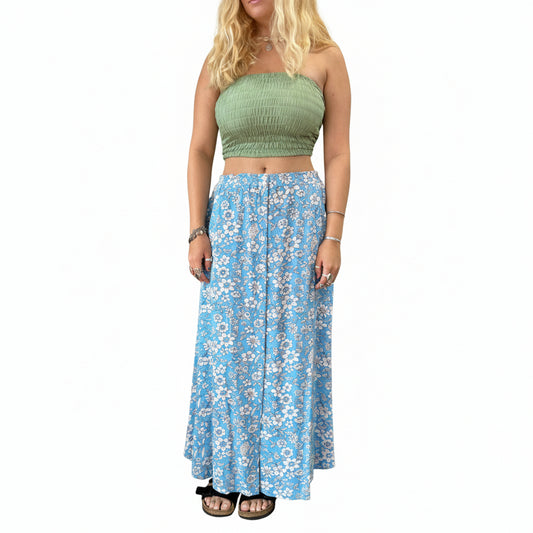 Person wearing a green top and blue floral skirt in a store setting with plants and shelves.