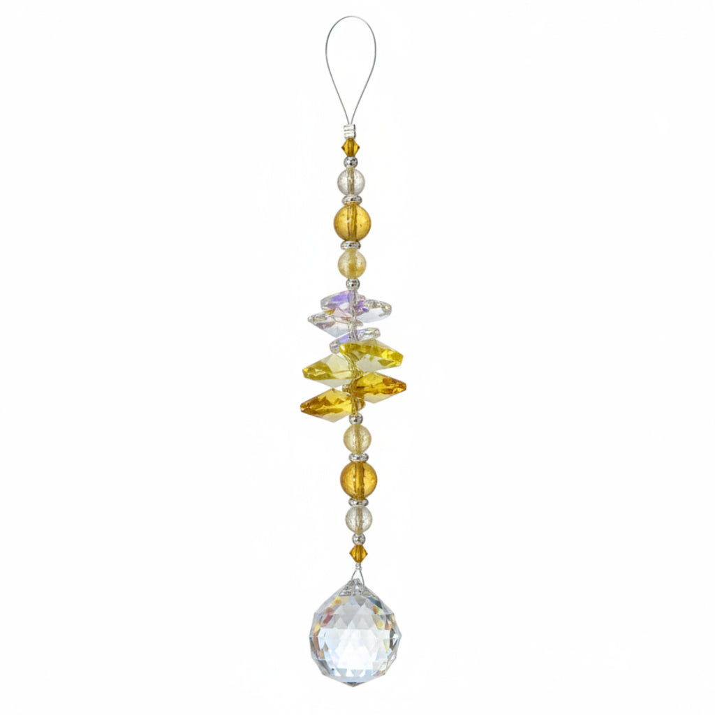 A hanging crystal ornament with a large faceted clear crystal pendant, yellow and amber crystal beads, and a small printed tag at the top, photographed on a wooden surface.