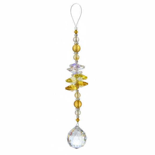 A hanging crystal ornament with a large faceted clear crystal pendant, yellow and amber crystal beads, and a small printed tag at the top, photographed on a wooden surface.