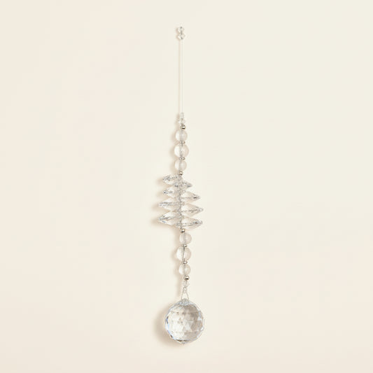 A clear crystal wind chime ornament with a hanging tag, displayed on a brown wooden floor.