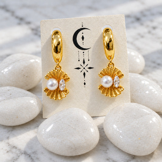 Gold earrings with pearls on a display card, placed on a white stone surface.
