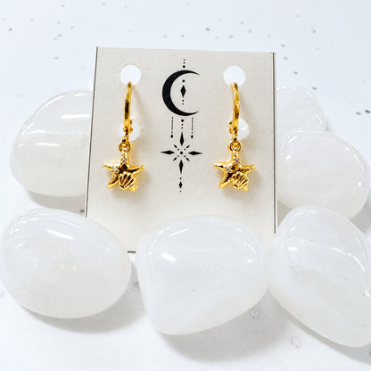 Gold star-shaped earrings on a card with white stones in the background