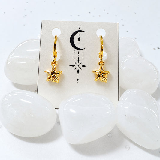 Gold star-shaped earrings on a card with white stones in the background