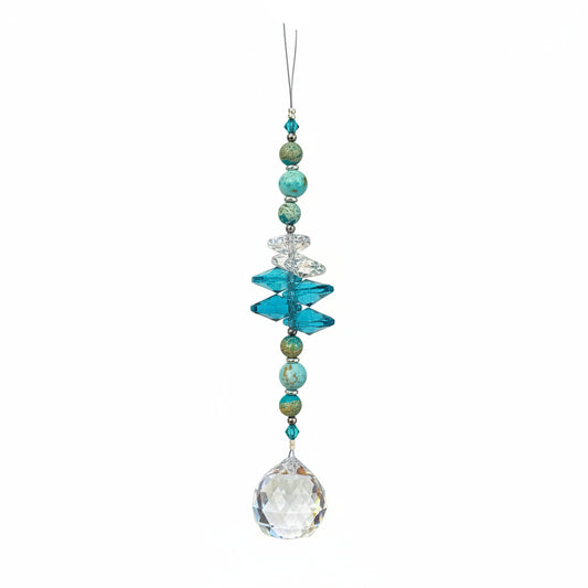 A beaded crystal suncatcher ornament with turquoise, blue, and iridescent beads, hanging on a wooden floor.