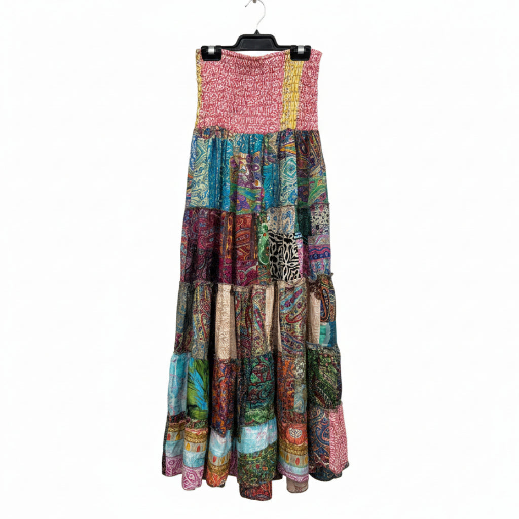 A sleeveless tiered maxi skirt made of many colorful patchwork fabric panels, hanging on a black hanger inside a clothing store.