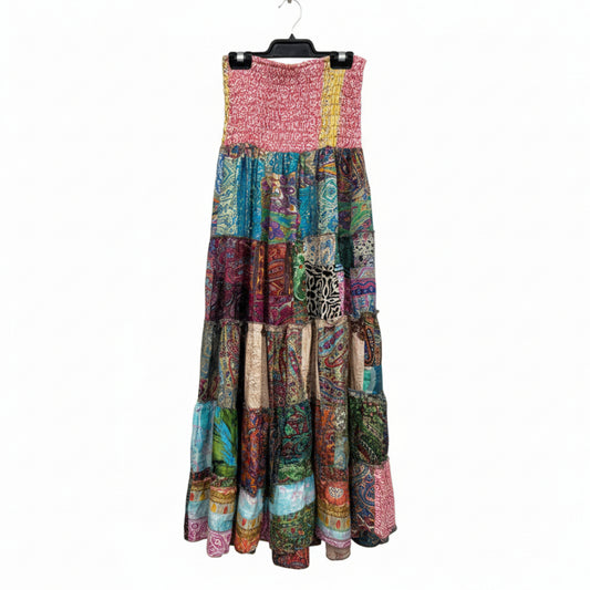 A sleeveless tiered maxi skirt made of many colorful patchwork fabric panels, hanging on a black hanger inside a clothing store.