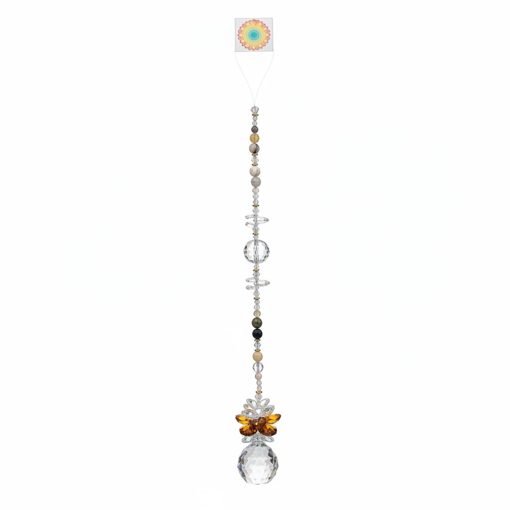 A beaded crystal suncatcher or wall hanging with iridescent and translucent beads, a butterfly charm, and a large faceted clear crystal ball at the bottom, laid flat on a brown wood floor.