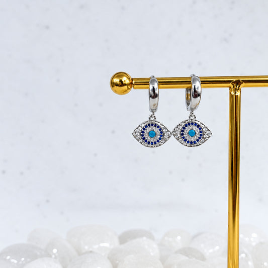 Silver earrings with blue stones on a gold stand against a white background