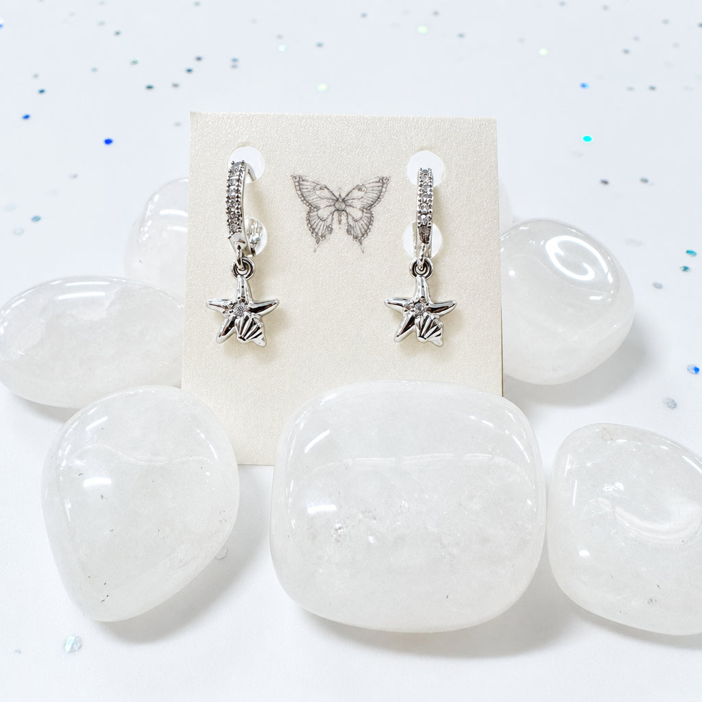 Silver starfish earrings on a display card with clear stones on a speckled surface