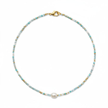 Close-up of a person wearing a necklace with a pearl pendant in an indoor setting.