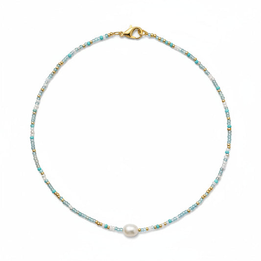 Close-up of a person wearing a necklace with a pearl pendant in an indoor setting.