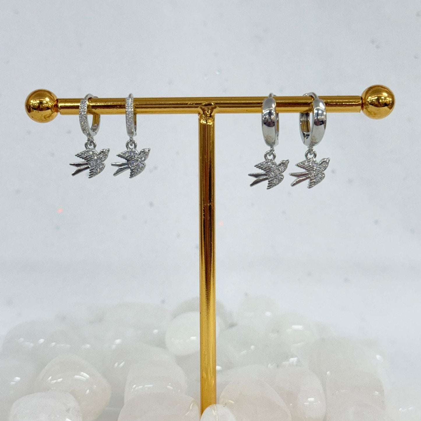 Silver earrings with leaf designs on a gold display stand against a white background.