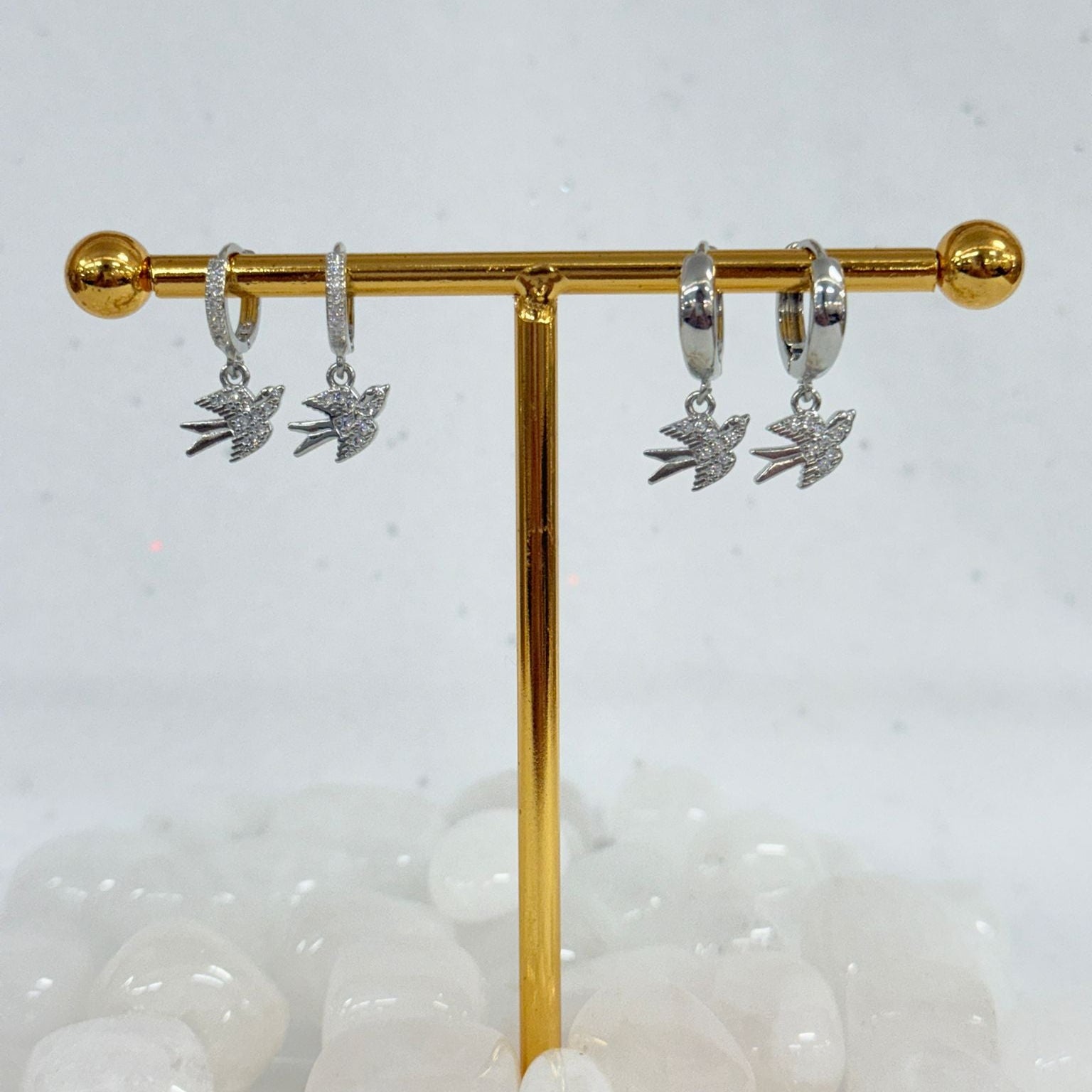 Silver earrings with leaf designs on a gold display stand against a white background.