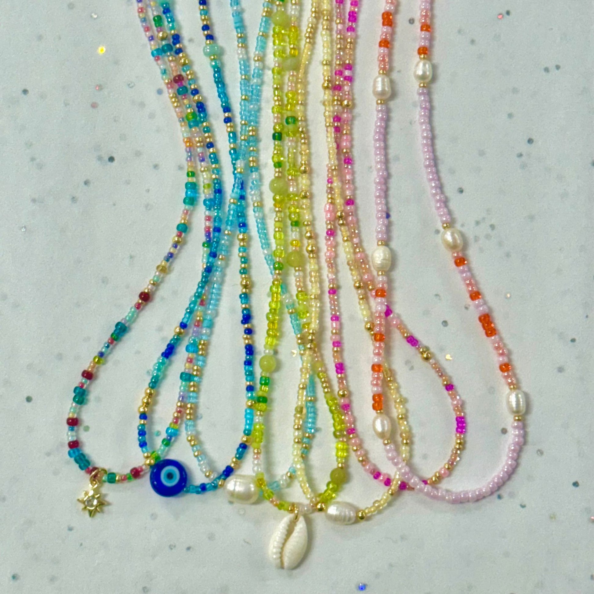 Colorful beaded necklaces with various pendants on a light gray background
