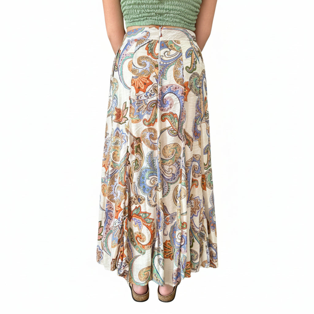 Person wearing a green top and colorful paisley skirt in a store setting with plants and decor.
