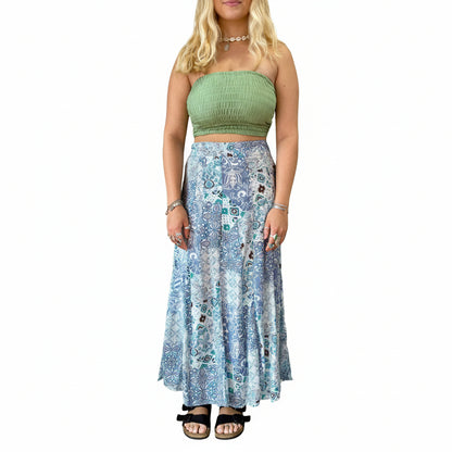 Woman wearing a green top and blue patterned skirt in a room with plants and decor.