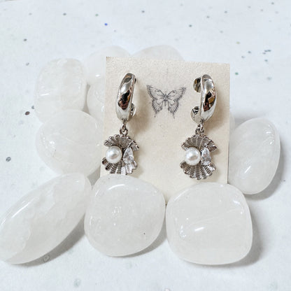 Pair of earrings with pearl-like charms on a white stone surface