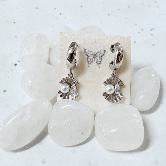 Pair of earrings with pearl-like charms on a white stone surface