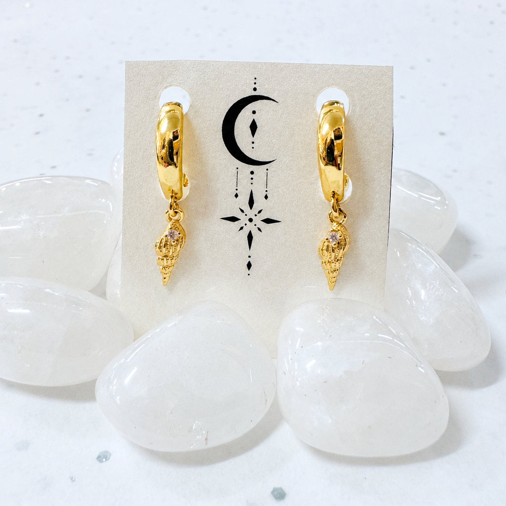 Gold hoop earrings with a small pendant on a display card, surrounded by white stones.