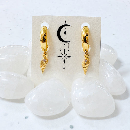 Gold hoop earrings with a small pendant on a display card, surrounded by white stones.