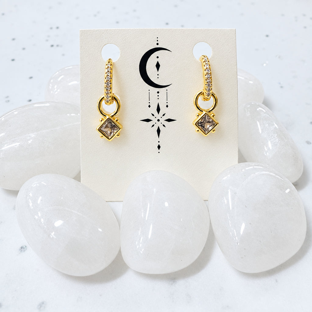 Gold earrings on a card with crystals in the background