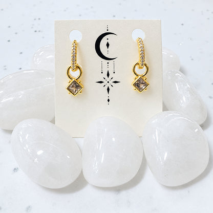 Gold earrings on a card with crystals in the background