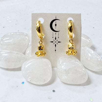 Gold hoop earrings with white stones on a beige card against a light gray background