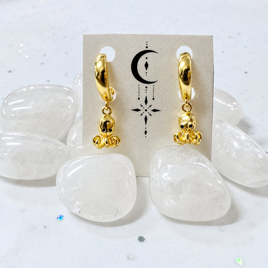 Gold hoop earrings with white stones on a beige card against a light gray background
