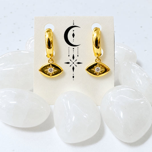 Gold hoop earrings with gemstones on a display card, surrounded by white stones on a light background.