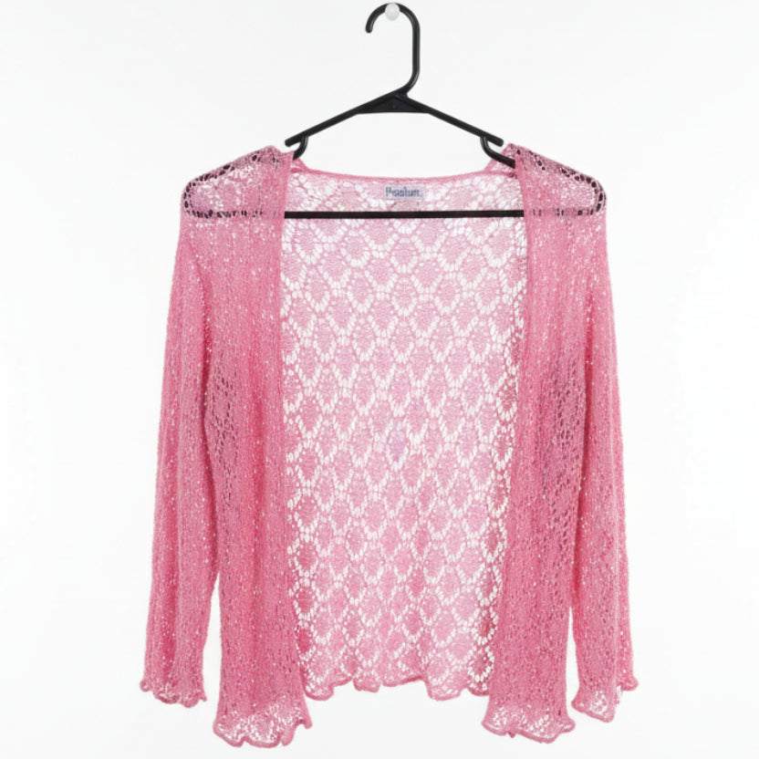 A pink open-front crochet cardigan with three-quarter sleeves hanging on a black hanger in a clothing store. A white price tag is visible near the neckline.