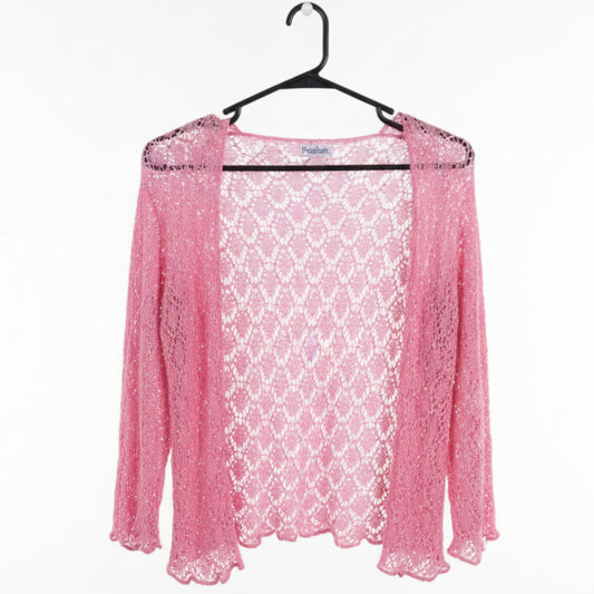 A pink open-front crochet cardigan with three-quarter sleeves hanging on a black hanger in a clothing store. A white price tag is visible near the neckline.