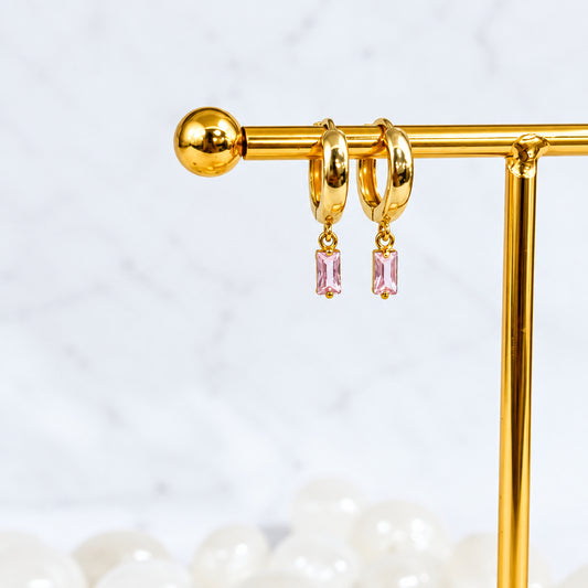 Gold hoop earrings with pink gemstones on a gold stand against a light gray background