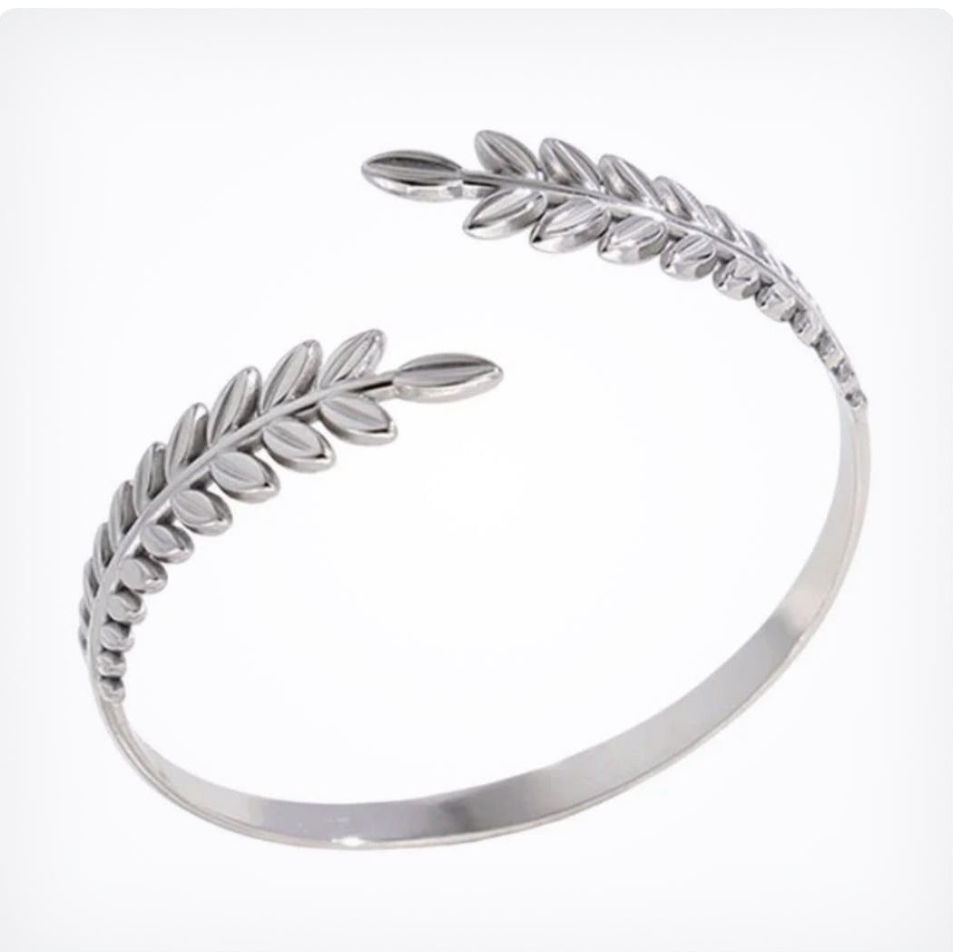 A polished silver open cuff bangle featuring detailed leaf and olive branch motifs on each end, displayed on a clean white background.