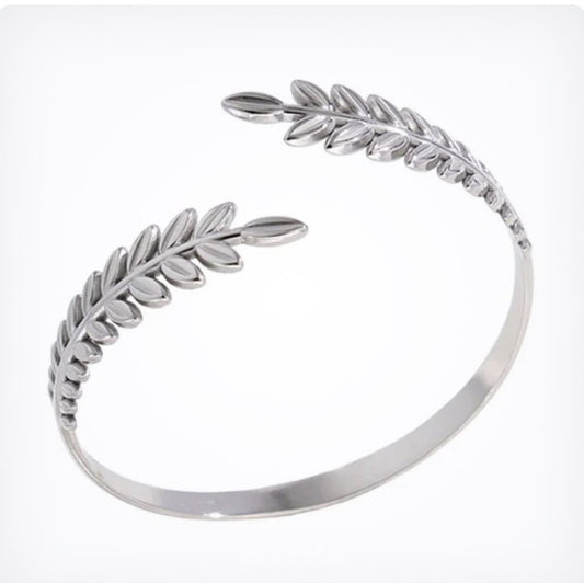 A polished silver open cuff bangle featuring detailed leaf and olive branch motifs on each end, displayed on a clean white background.