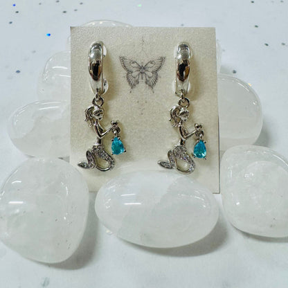 Pair of earrings with boot charms on a display card with butterfly design, placed on a white stone surface.