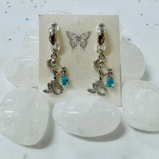 Pair of earrings with boot charms on a display card with butterfly design, placed on a white stone surface.