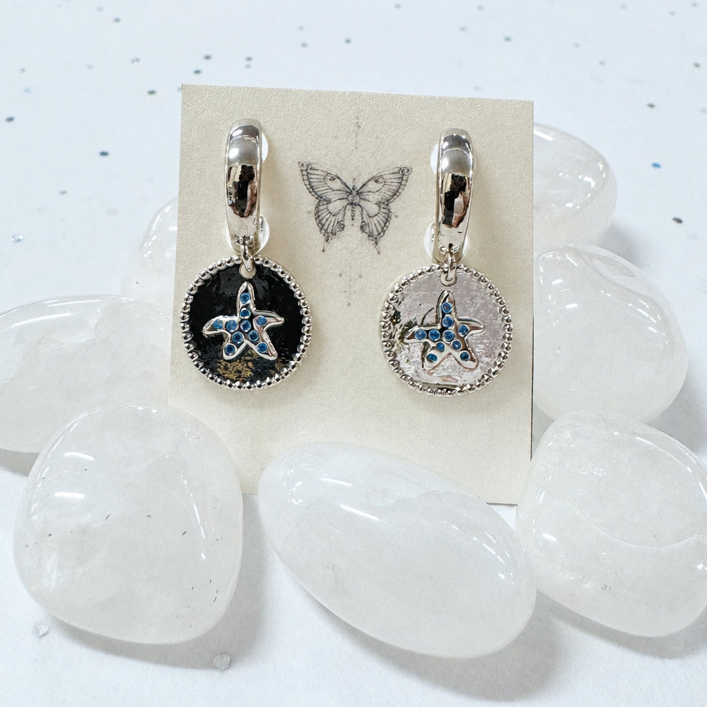 Starfish-themed earrings on a card with butterfly illustration, placed on clear stones.