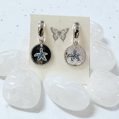 Starfish-themed earrings on a card with butterfly illustration, placed on clear stones.