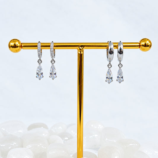 Gold earring stand with silver earrings on a white stone surface