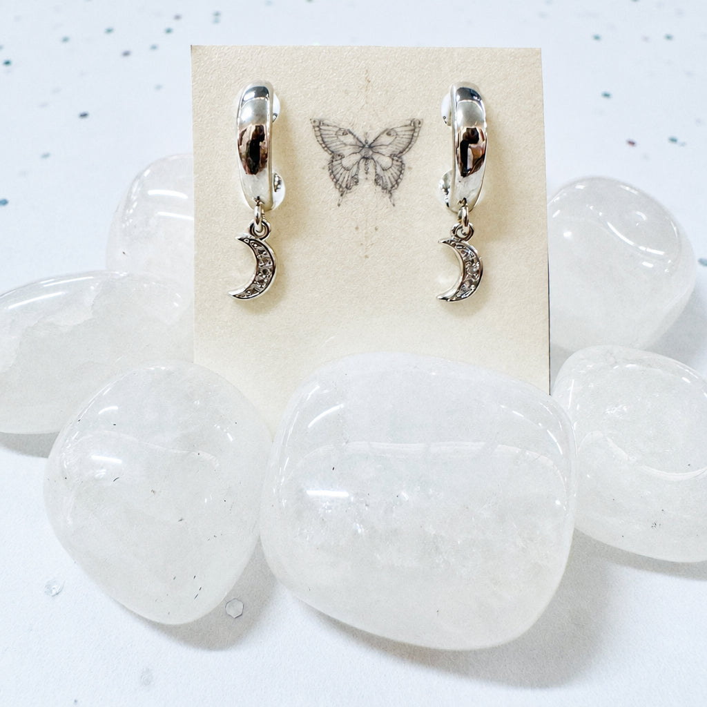 Pair of earrings with moon designs on a card, displayed on a white stone surface.