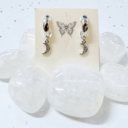 Pair of earrings with moon designs on a card, displayed on a white stone surface.